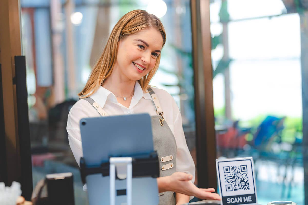 Camarera sonriente con delantal mostrando código QR en el mostrador